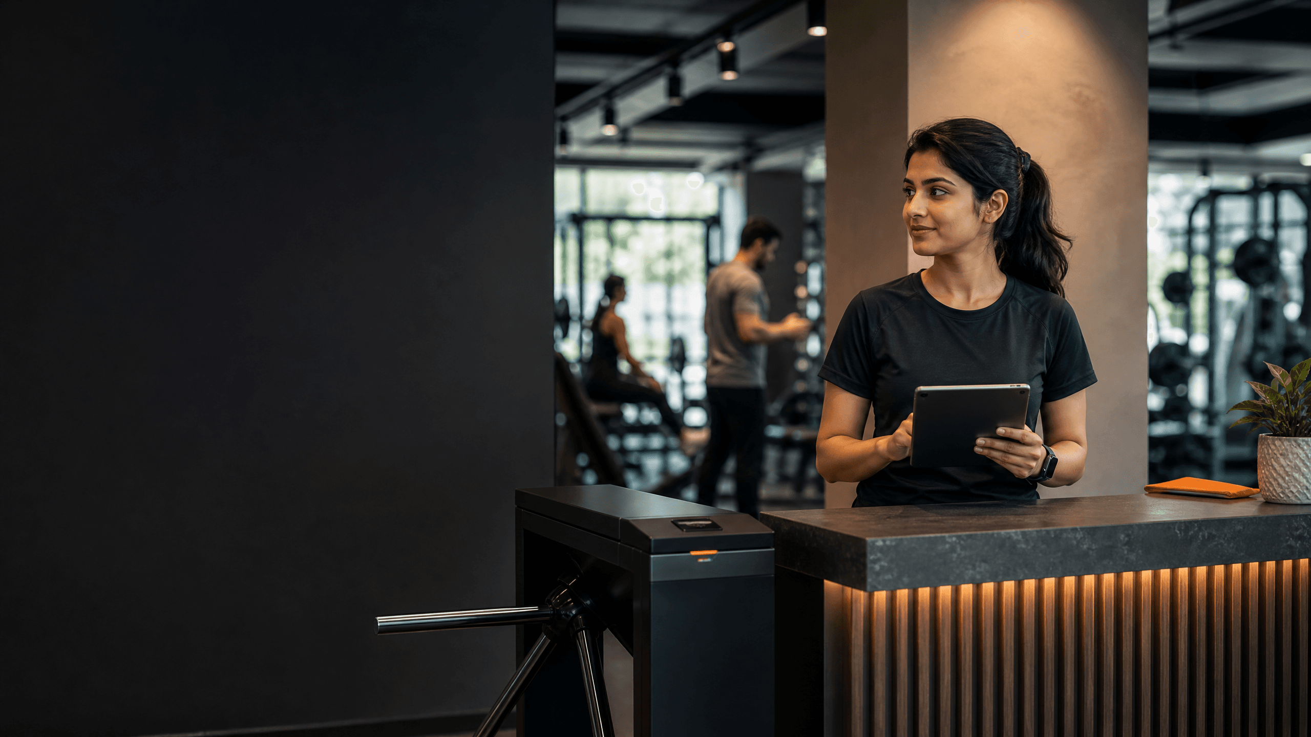 A gym receptionist using GymSuite on a tablet at the front desk